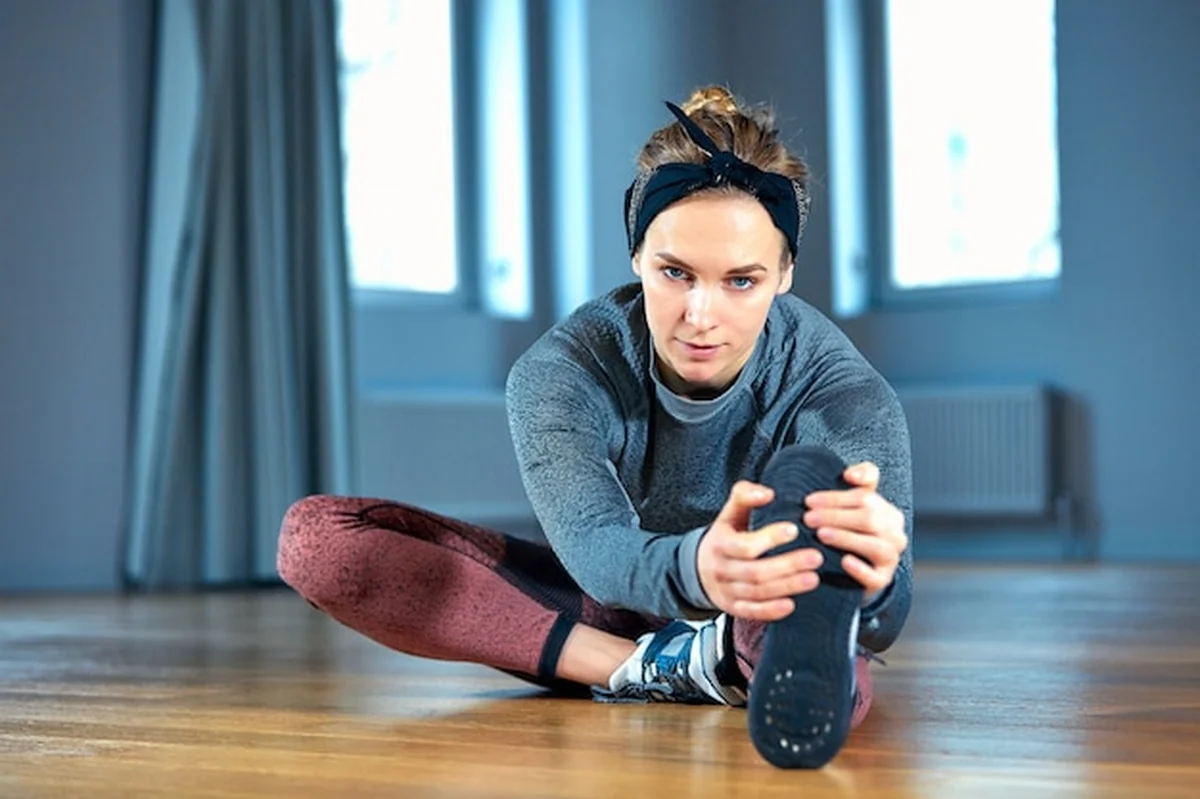 Młoda kobieta w sportowej robi rozciąganie na podłodze przed oknem w siłowni